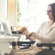 A person in an electric wheelchair is typing on a laptop. She has shoulder length hair.