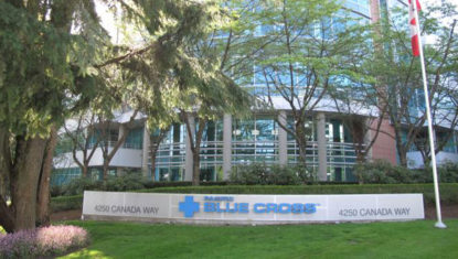 The Pacific Blue Cross Head Office, in Burnaby. A cement block spells out their name, with trees surrounding it.