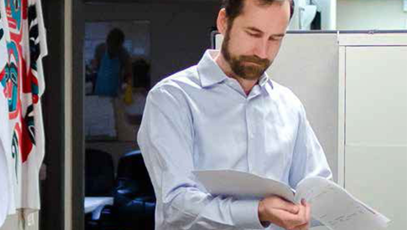 A business leader is standing in his office, reviewing a document.