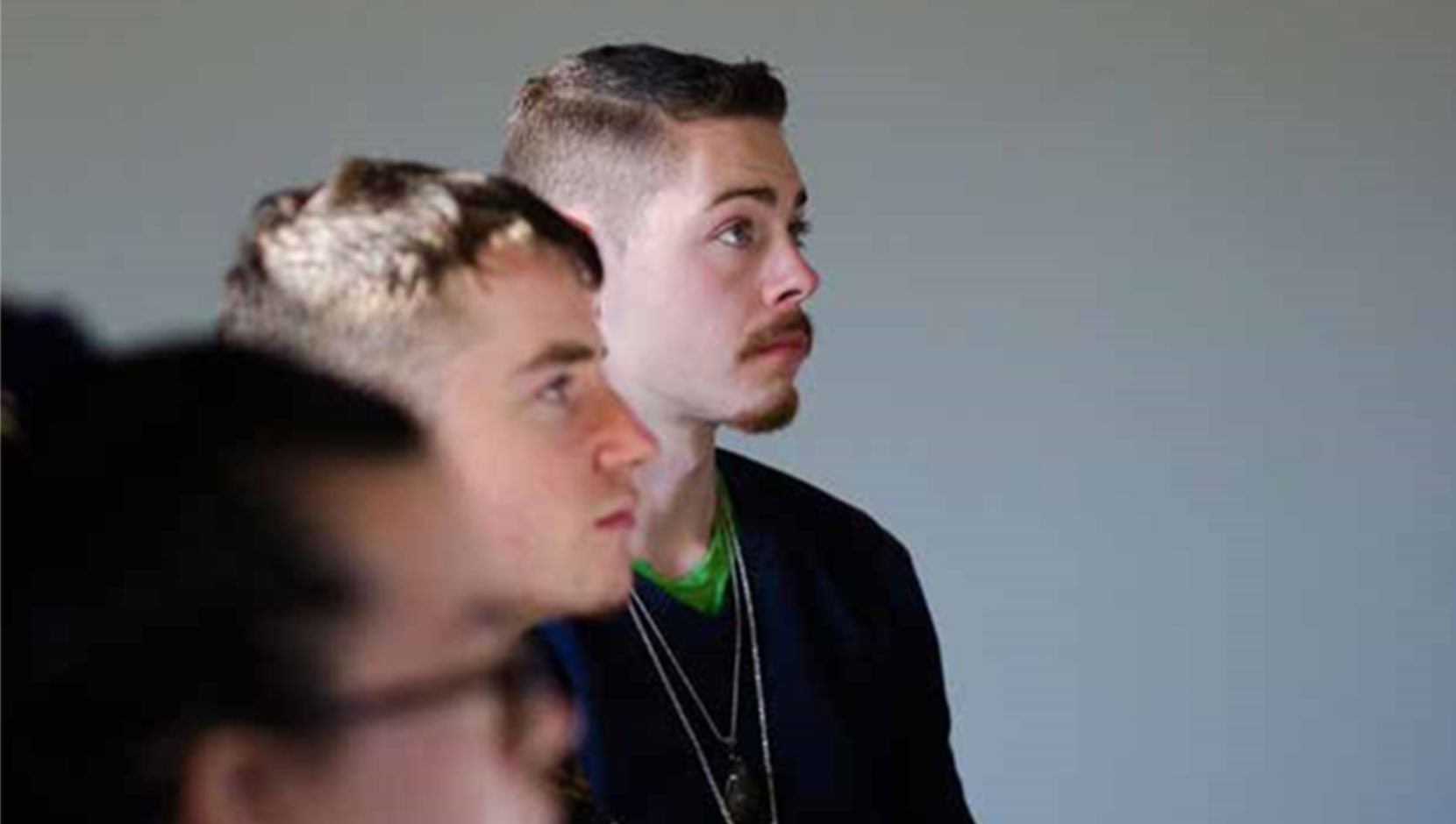 Image of three white employees listening to someone speak and all looking forward. Photo is taken from the side.