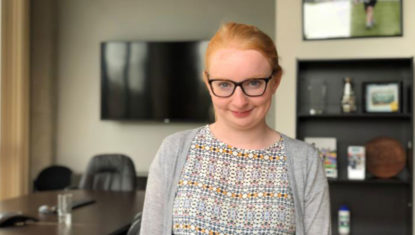CAN employee Siobhan smiles at the camera. She is a white woman with red hair pulled back, wearing black glasses.