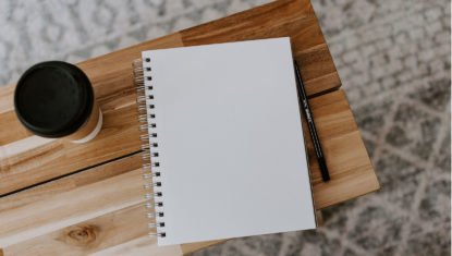 A blank notebook open on a wooden table, with a coffee to the left.