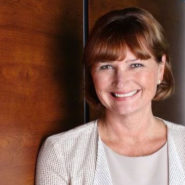 Headshot of Marsha Walden. She has on a cream top and blouse, with short brown hair. She is smiling and up against a brown wall.