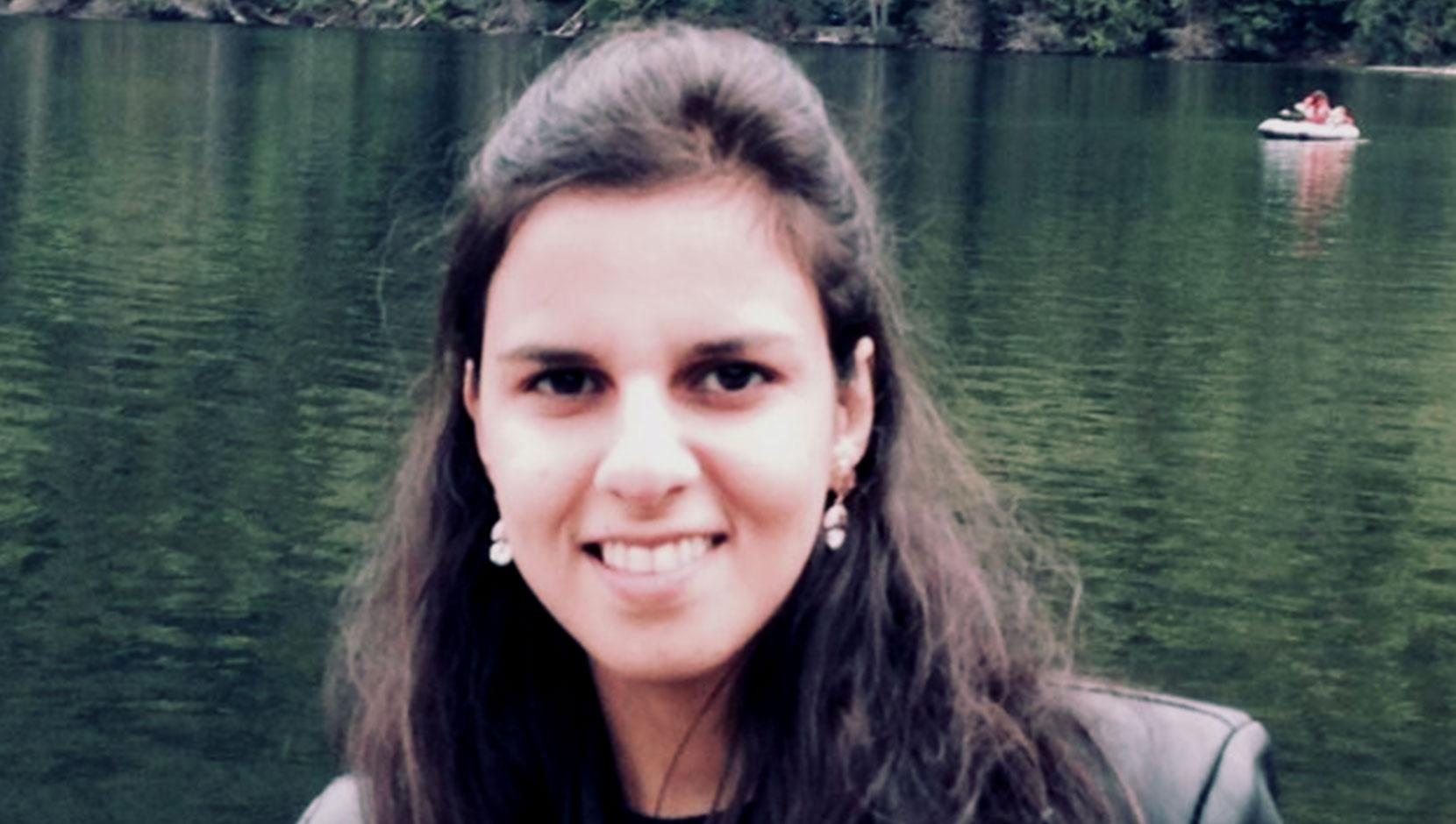 Mehrnoush smiling at the camera. She is in front of a body of water, with shoulder length brown hair pulled back partially.