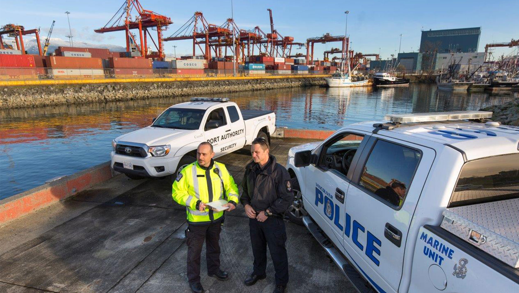 A Port Authority security person and Vancouver Police person both stand outside their trucks by the water outside the Port Authority.