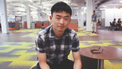 Matthew Huang of SAP. He is seated on a round chair at SAP's Vancouver office, with colourful patterned floor all around. He is an Asian man with short dark hair, and a short sleeve top.