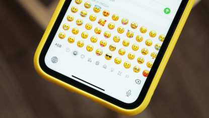 An iphone with a yellow case is open to a text message screen, with the emoji library visible.