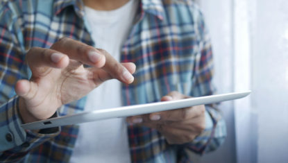 Person in red and blue plaid shirt holding a tablet.