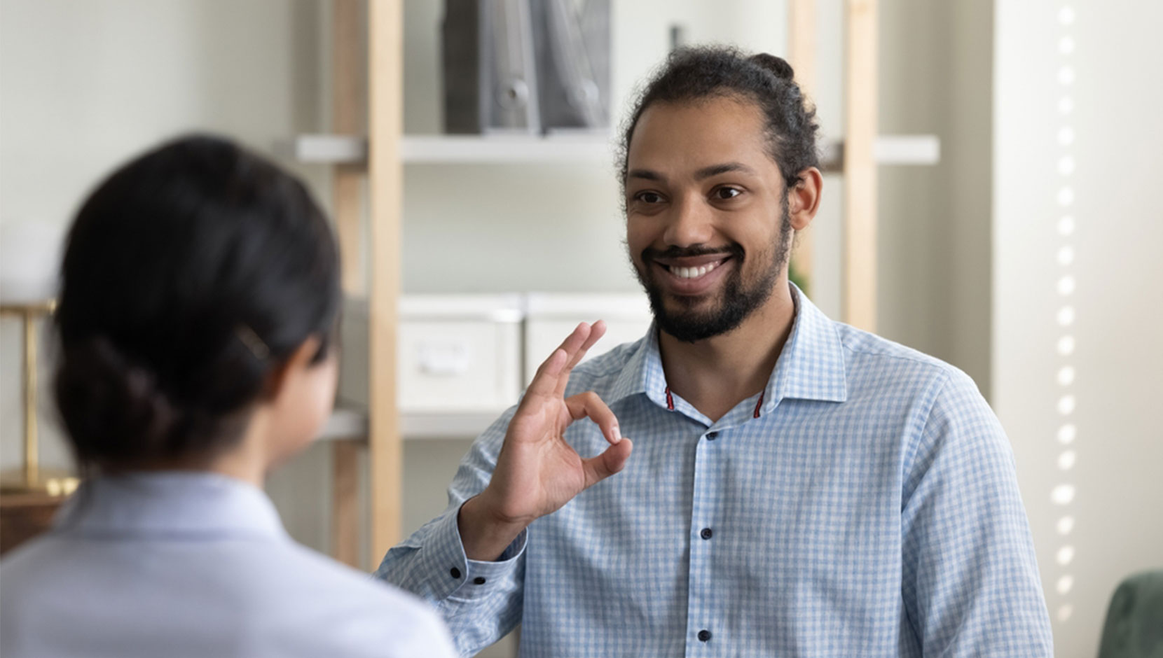 A person of colour is facing the camera, smiling, and signing in ASL.