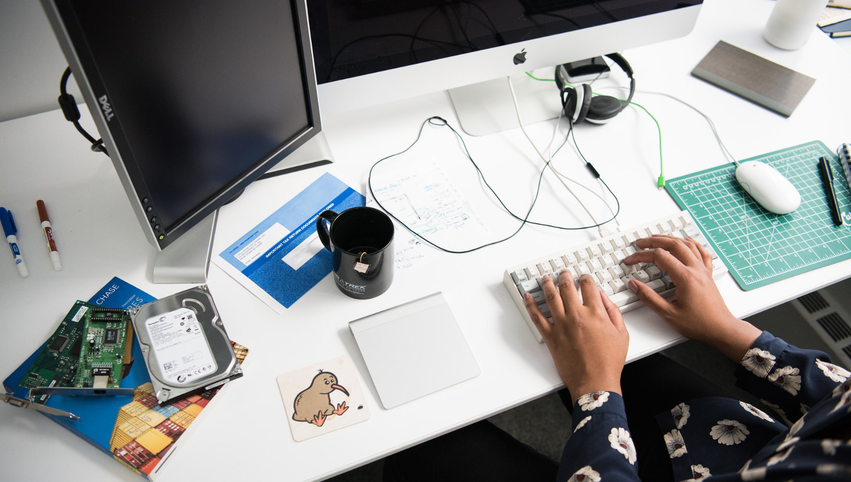 A person of colour's hands typing on a keyboard in front of two monitors.