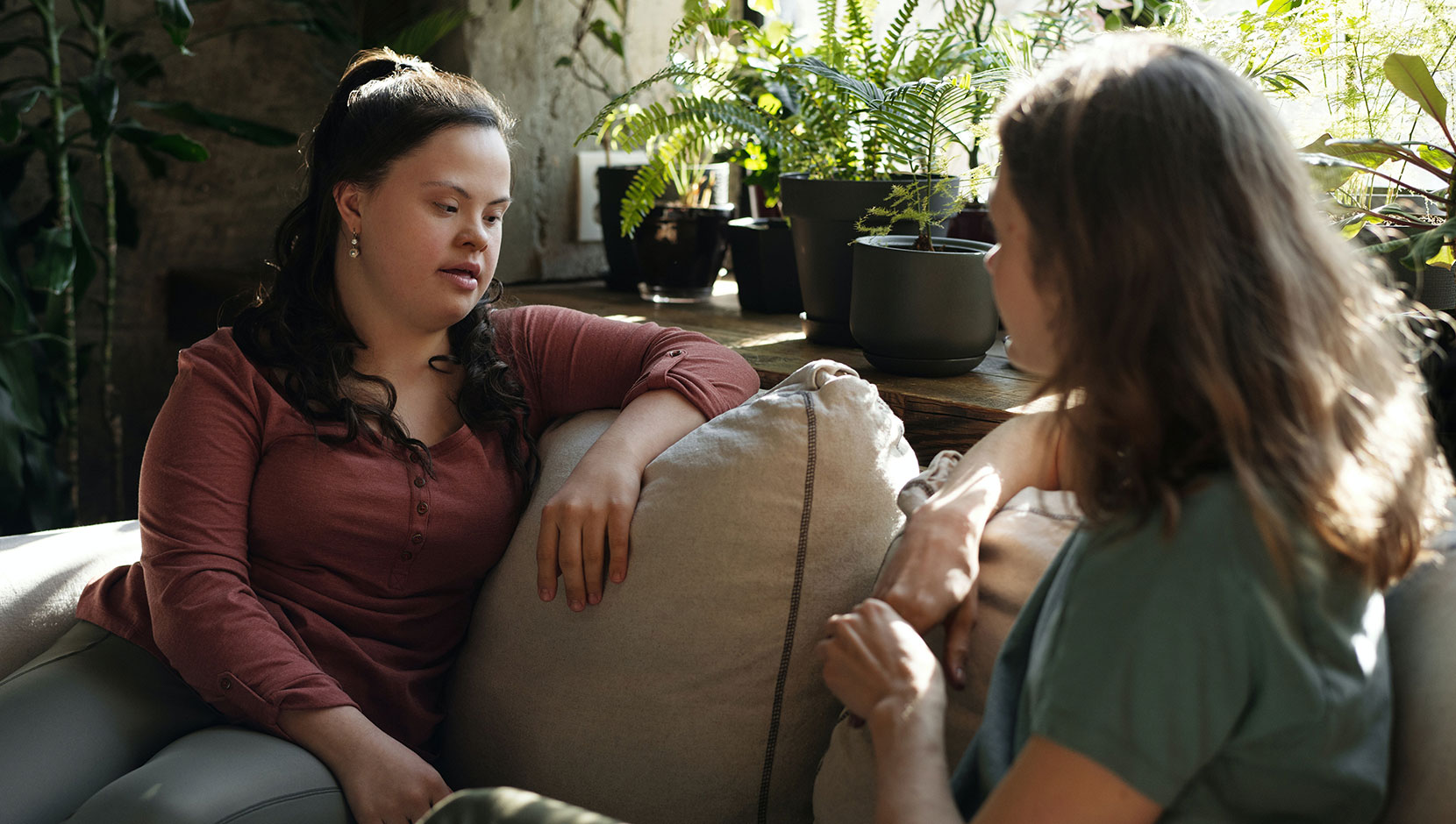 Two women seated on a couch in conversation. The one on the left has Down syndrome.