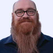 Headshot of Aaron Cruikshank. He is a white man with receeding hair and a full, long red beard and glasses. He is wearing a navy collared shirt.