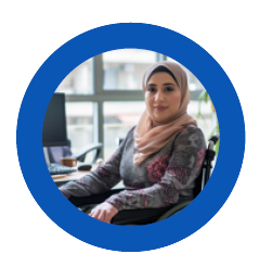 A person wearing a pink hijab is seated in a wheelchair in a work setting.