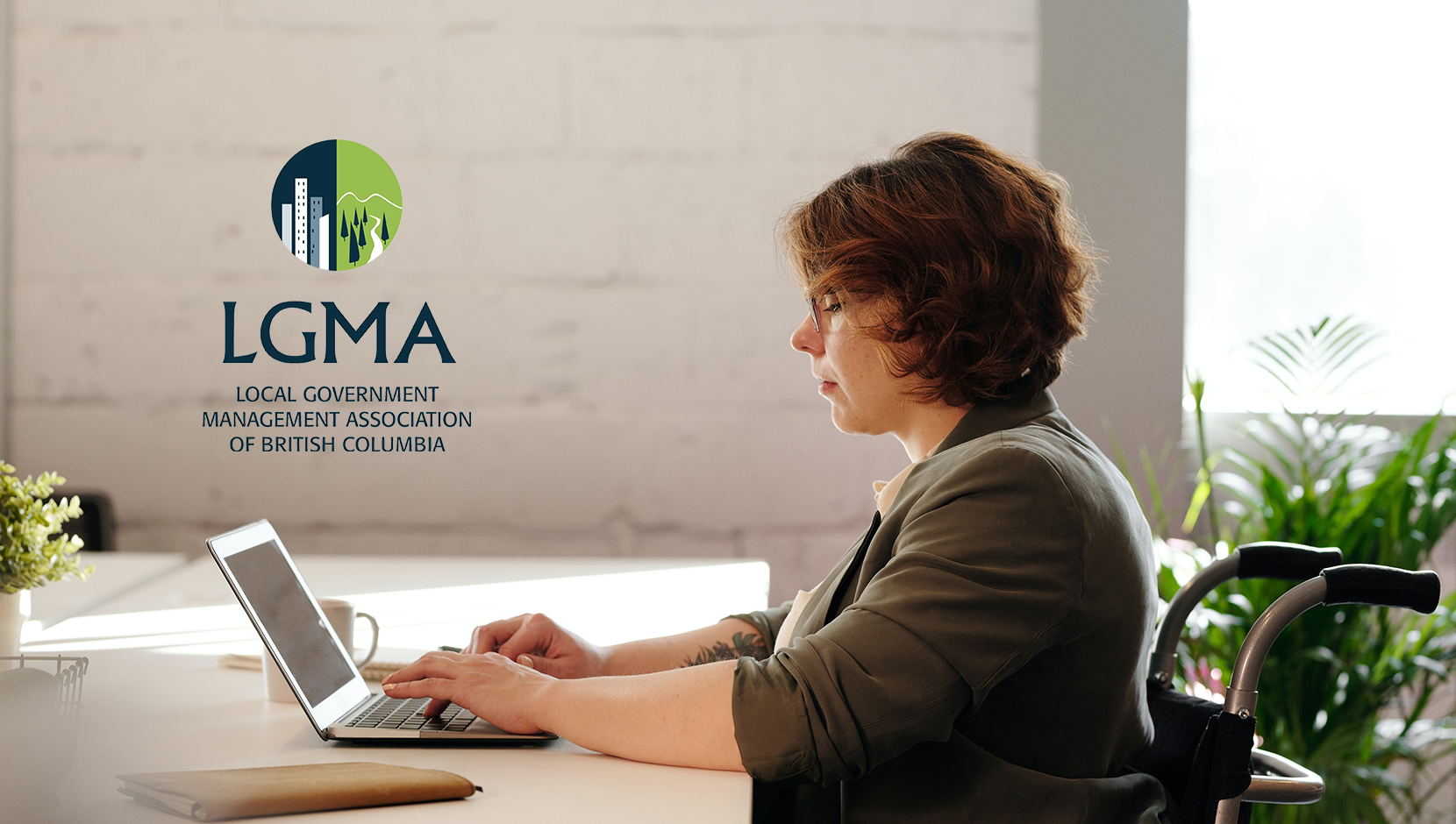 A white woman in a manual wheelchair with short red hair is working on a laptop. LGMA BC logo overlaid.