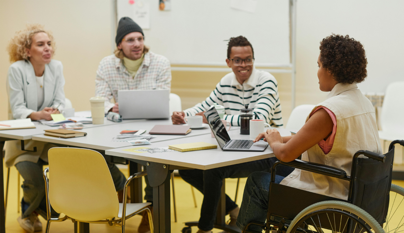 A group of colleagues gathered at a table. The person on the far right is in a manual wheelchair.