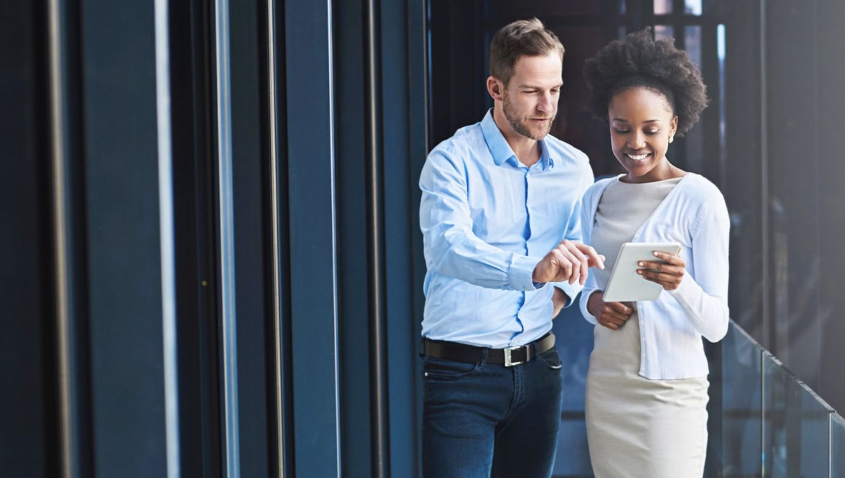 Two people in business clothing are looking at an iPad held by the person on the right.