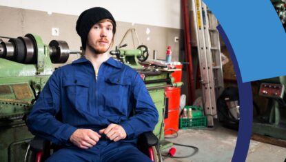 A person in a manual wheelchair is wearing a mechanic uniform and working at a service repair facility.