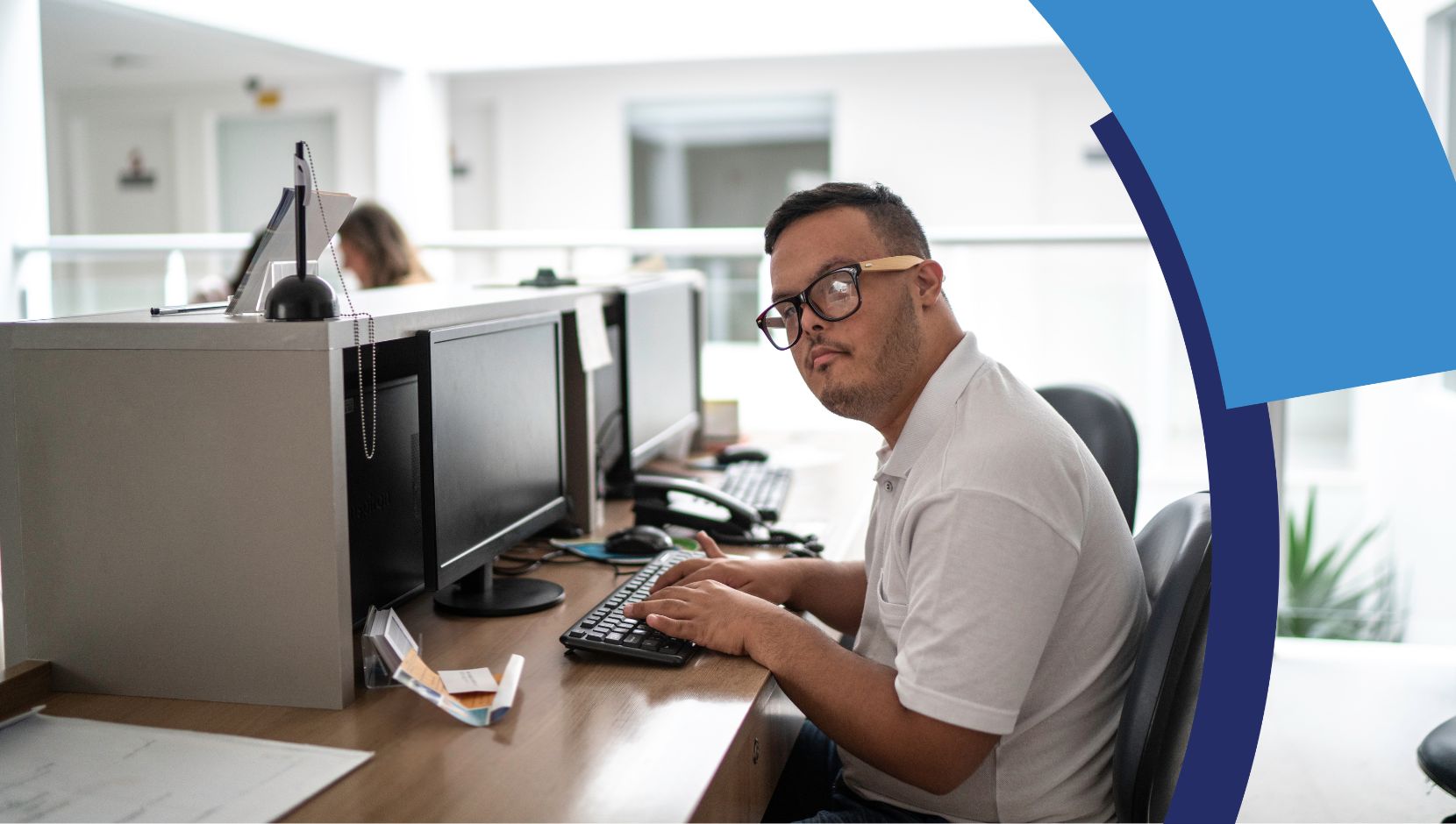 A young person with Down syndrome is seated at a workstation typing on a computer.