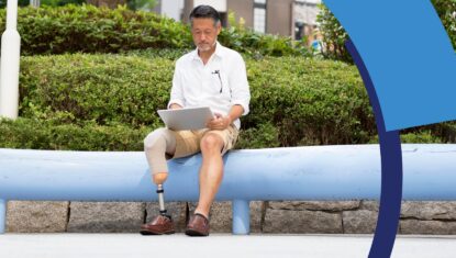 A middle-aged person with a prosthetic leg sits outside while doing work on a digital tablet.